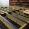 Deck joists taped along their tops during framing, with a flashed ledger against a Berkeley home in morning fog