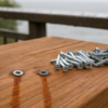 Rust streaks around screw heads on a redwood deck board with stainless and galvanized deck fasteners beside them