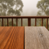 Redwood deck board showing sun-faded gray on one side and rich color in shade, with fog behind the railing