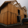 Rain-soaked plywood sheathing on an open house frame with water staining along panel seams and cut edges