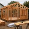 Partly framed backyard ADU in a Berkeley yard with stacked lumber and an extended tape measure on sawhorses